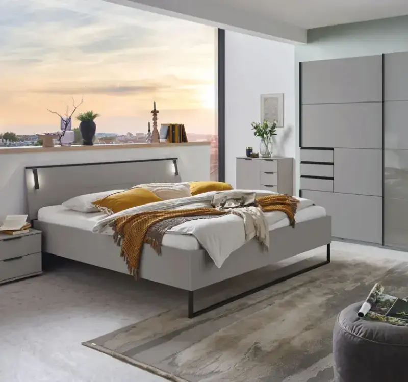 Schlafzimmer mit grauem Bett und Kopfteil, gelben Kissen und Decke, links bodentiefes Fenster mit Stadtblick, rechts grauer Kleiderschrank und Kommode.